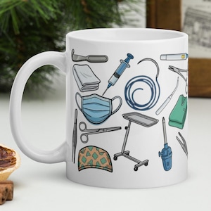 Könnte beinhalten: Weiße Keramiktasse mit einem Muster aus medizinischen Werkzeugen, darunter eine Spritze, eine OP-Maske und chirurgische Instrumente. Die Tasse ist mit blauen, grünen und grauen Illustrationen verziert, ideal für medizinisches Fachpersonal.