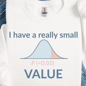 May include: White long-sleeve shirt with the text "I have a really small value" and a bell curve graphic. The shirt is laid on top of blue jeans. The text and graphic are in shades of blue and pink.