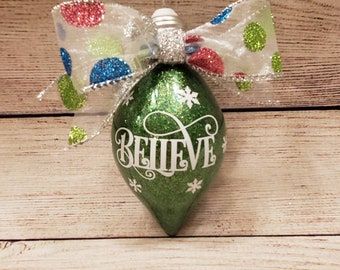 Green glittered light bulb shaped ornament with the word Believe on front and a polka dot glittered bow can be personalized w/ name on back