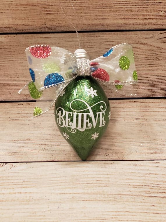 Green glittered light bulb shaped ornament with the word Believe on front and a polka dot glittered bow can be personalized w/ name on back