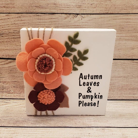 White shelf/desk sign with felt flowers in apricot, rust and maroon, felt leaves and twine. With the words Autumn Leaves & Pumpkin Please.