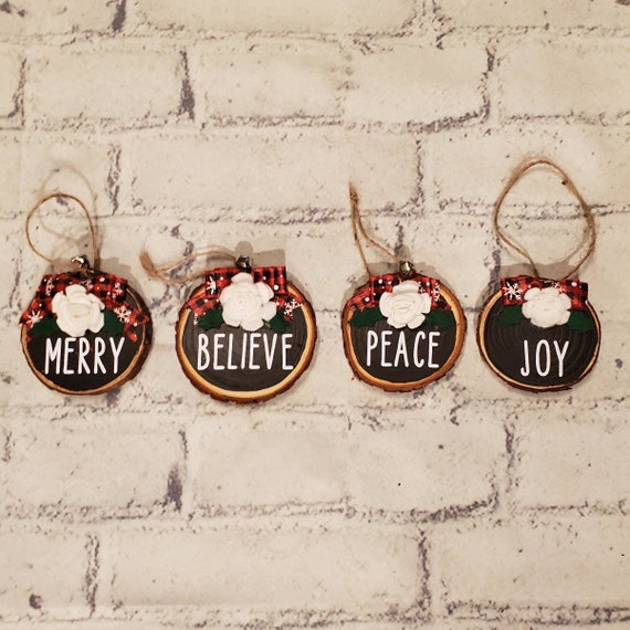 Set of 4 wood slice ornaments painted black with a handmade red felt flower and buffalo check bow and the words Joy Peace Believe and Merry