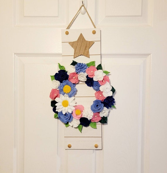 Wall decor white wood slat sign with a wood star on top and a felt flower wreathade with 25 handmade felt flowers in pink, blues, and white