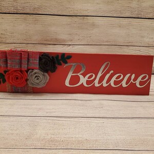 Painted red wood shelf sitting sign handmade felt flowers and with burlap and grey and red plaid bow and the metal cutout word Believe
