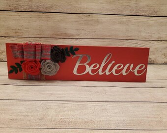 Painted red wood shelf sitting sign handmade felt flowers and with burlap and grey and red plaid bow and the metal cutout word Believe