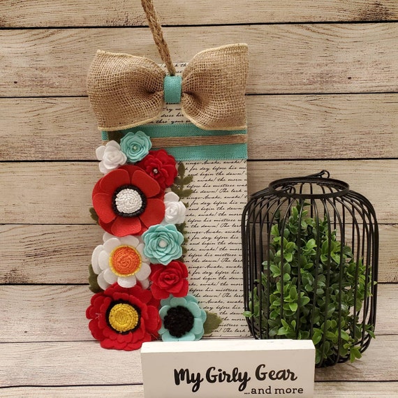 Felt flower sign inred and mint tag shaped thin wood decoupaged with script paper on front felt on back hanging from braided twine.