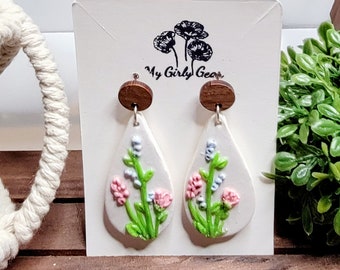 Blue and pink flowers on a white teardrop background.  Hand sculpted flowers in polymer clay Surgical steel dangle earring style of choice.