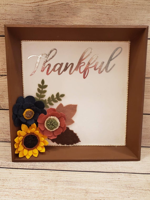 Rustic Thankful sign with metal cutout and hand made felt flowers and leaves on a white background with a pearl trim accent and brown frame