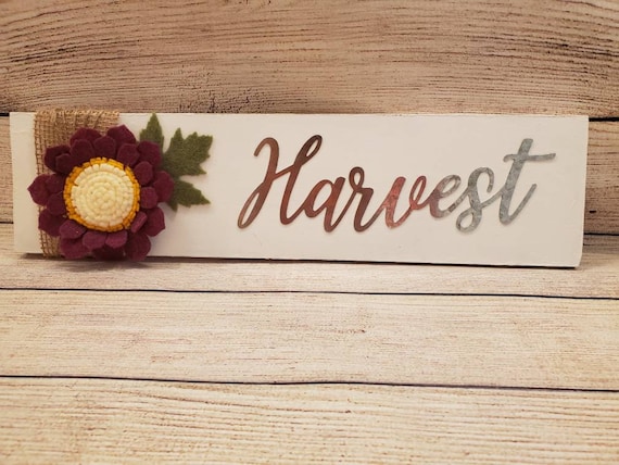 Wood sign painted white with handmade burgundy felt flower,  green leaf, the word Harvest in metal with bulap and twine wrapped on one side.