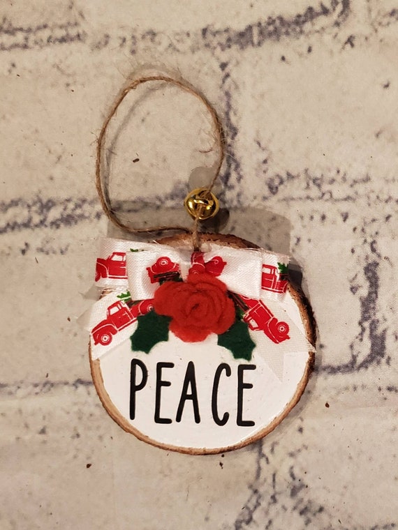 3 inch Wood slice ornament painted white with handmade red felt flower and green holly, a red truck bow and the word Peace in the center.