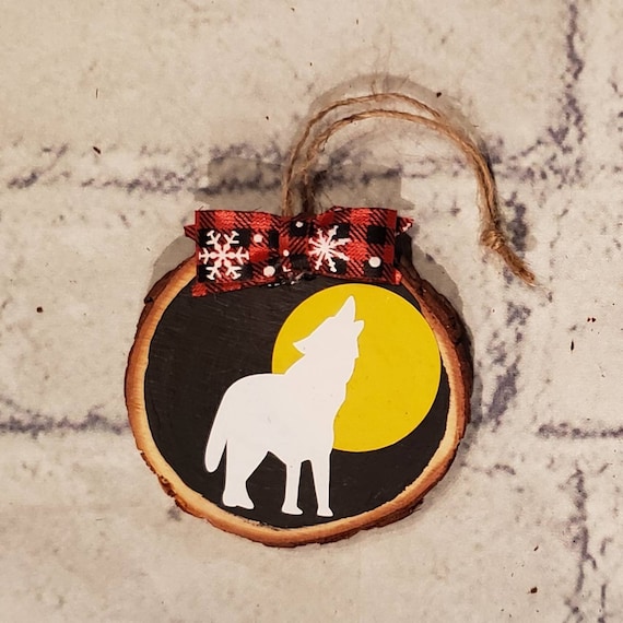 3 in. wood slice ornament painted black with a handmade buffalo check bow, twine to hang from and a yellow moon and white wolf in vinyl.