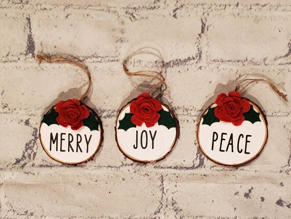 Set of 3 wood slice ornaments painted white with handmade  felt red flowers and green holly the word Joy Peace and Merry and hung with twine