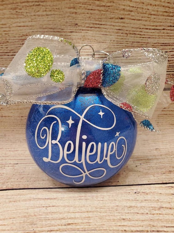 3 1/2 inch blue glittered disk ornament with a polka dot glittered bow and the word Believe on front Can be personalized with name and year