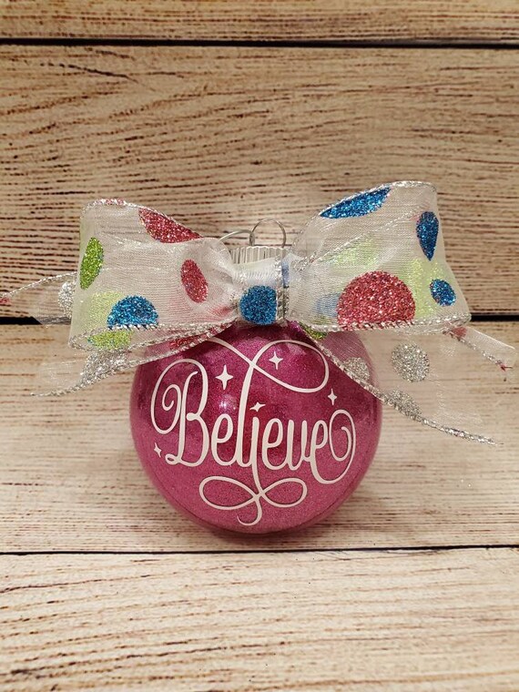 3 1/2 inch pink glittered ornament with the word Believe on front with a polka dot glittered bowon top and can be personalized on back.