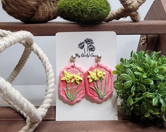 Cute yellow daffodils on a dark and light pink marbled framed background.  Hand sculpted flowers and leaves Surgical steel dangle earrings