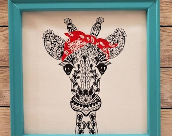 12×12in. Canvas with frame with a sassy giraffe mandala wearing a red bandana in a teal wood frame.