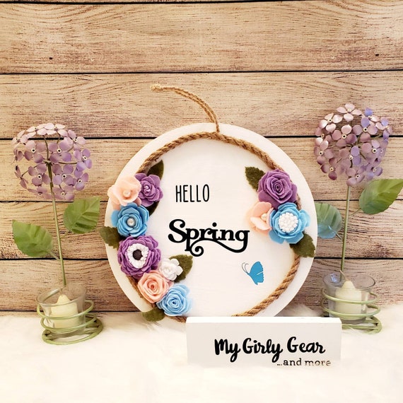 Hello Spring round sign pastel felt flowers in pink lavender and blue and a rope ring. Painted white with black writing 12 inch.