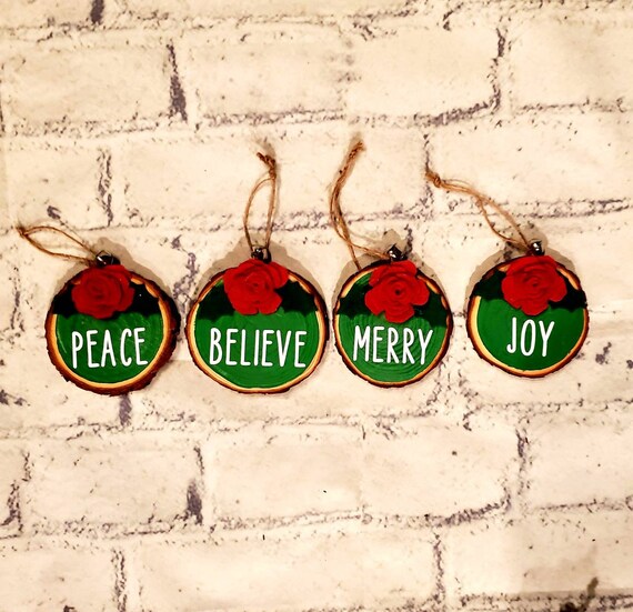 4 wood slice green painted ornaments with a handmade felt flower and holly leaves, The words " Peace, Joy, Believe and Merry" on its center.