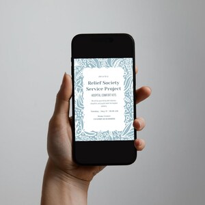 May include: A black smartphone shows a light blue and white invitation for a Relief Society Service Project. The invitation includes text about Hospital Comfort Kits and event details. The phone is held in a hand against a neutral background.
