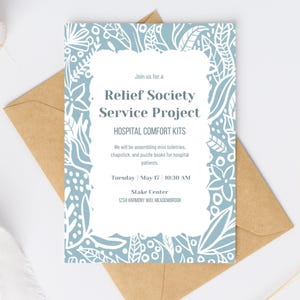 May include: An invitation for a Relief Society Service Project, Hospital Comfort Kits. The invitation has a light blue floral design with white accents. The text includes the date, time, and location of the event. The invitation is placed on a brown envelope.