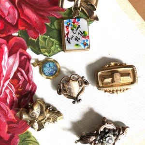 May include: A collection of antique gold-toned brooches and pins. Includes a bow-shaped pin, a book-shaped pendant with floral accents and the text "Pine Camp N.Y.", a shield-shaped pin, and other ornate designs.