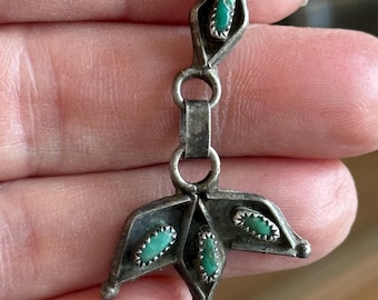 Op de afbeelding: Een zilverkleurige hanger met een bloemmotief. De hanger heeft drie turquoise gekleurde stenen gezet in een gestileerde bladvorm en een turquoise steen in een ruitvormig bovenelement.