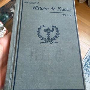 May include: A vintage book titled "Histoire de France" by Wright, with the author's name and the title in black text on a gray cover. The cover features a decorative emblem and a dark blue border.