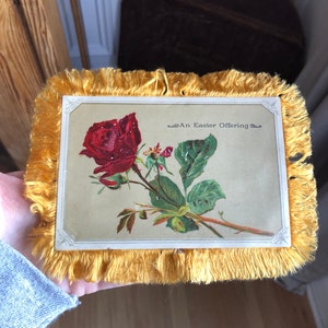 May include: A vintage Easter card with a red rose and green leaves. The card has a yellow fringe border and the text "An Easter Offering" in the top right corner.