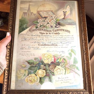 May include: A vintage Confirmation Certificate in a decorative gold-toned frame. The document features an open Bible, a chalice, and illustrations of white and yellow roses. Text includes "Confirmation Certificate," "This do in remembrance of Me," and "The fear of the Lord is the beginning of Wisdom."