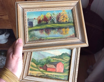May include: Two framed paintings with gold trim. The top painting depicts a landscape with a house, trees, and a river. The bottom painting depicts a landscape with a red barn and rolling hills.