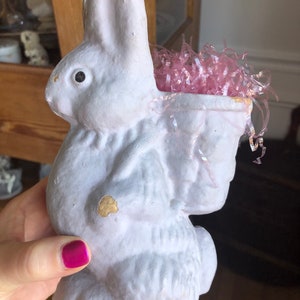 May include: A white paper mache bunny rabbit with a pink paper basket filled with pink shredded paper. The bunny has a black eye and is slightly chipped.