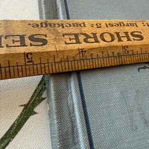 Puede incluir: Una regla de madera con marcas negras y el texto "SHORE SEI" se coloca sobre un libro azul claro. El libro tiene el t&iacute;tulo "Histoire de Fr" impreso en la portada. La regla mide hasta 12,7 cm.