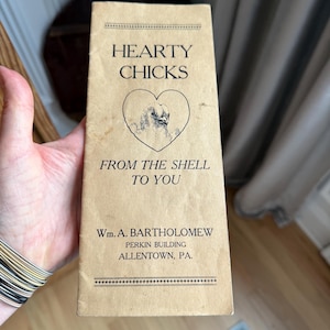 May include: A vintage brown paper pamphlet advertising "Hearty Chicks" from the shell to you. The pamphlet features a heart-shaped image of a chick and the text "Wm. A. Bartholomew, Perkin Building, Allentown, PA."