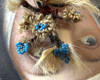 May include: A decorative hairwork piece featuring light brown hair woven into small floral shapes, accented with clusters of bright blue glass beads. The hair is wrapped around dark brown stems, creating a textured, multi-dimensional floral arrangement.