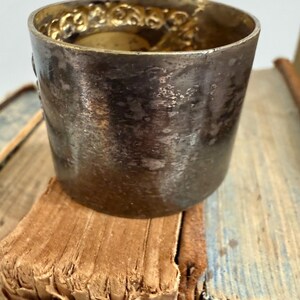 Puede incluir: Una peque&ntilde;a copa de plata antigua con un borde dorado decorativo y ornamentado. La copa es cil&iacute;ndrica y se apoya en una pila de libros viejos y desgastados. La superficie de la copa muestra signos de edad y uso.