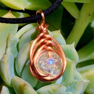 May include: A copper wire wrapped pendant with a iridescent white gemstone. The pendant is hanging from a black cord.