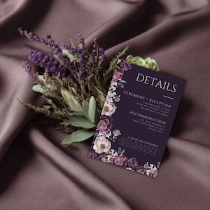 Può includere: Un biglietto d'invito viola scuro con decorazioni floreali e la parola "DETAILS" in alto. La carta include testo su una cerimonia, un ricevimento e un alloggio. Un bouquet di fiori e verde viola è posto accanto alla carta.