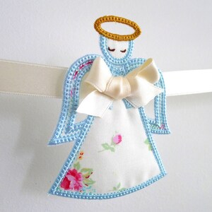 May include: A blue and white angel ornament with a gold halo and a white satin bow. The angel is embroidered with floral details and has a white background.