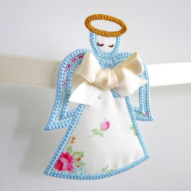 May include: A blue and white angel ornament with a gold halo and a white satin bow. The angel is embroidered with floral details and has a white background.