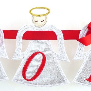 May include: A white Christmas banner with three angels holding the letters J, O, and Y. Each angel has a red bow and a gold halo. The banner is strung with red ribbon.