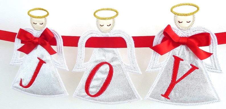 May include: A white Christmas banner with three angels holding the letters J, O, and Y. Each angel has a red bow and a gold halo. The banner is strung with red ribbon.