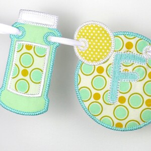 May include: A green and yellow fabric banner featuring the letter "F" and a jar design. The banner is decorated with a polka dot pattern.