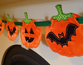 Könnte beinhalten: Ein Halloween-Banner mit orangefarbenen Filz-Kürbissen und einer schwarzen Filz-Fledermaus. Die Kürbisse haben grüne Filzstiele und aufgestickte Jack-o'-Lantern-Gesichter. Das Banner ist mit grünem Band aufgefädelt.
