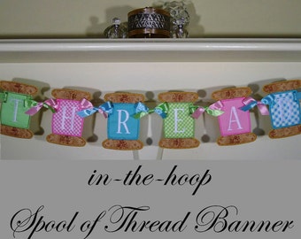 May include: A banner made of fabric spools with the word "THREAD" spelled out in pink, green, blue, and white letters. The spools are decorated with pink, green, and blue ribbon. The banner is labeled "in-the-hoop Spool of Thread Banner".