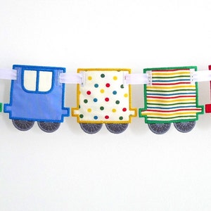 May include: A colorful train banner with five cars. The first car is green with a red, white, and blue striped chimney. The second car is blue, the third is yellow with red and green polka dots, the fourth is yellow with red and green stripes, and the fifth is red with a yellow and blue striped chimney.