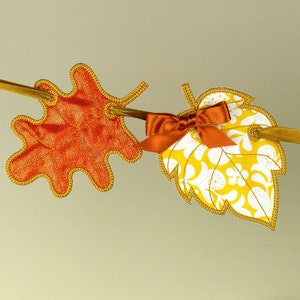 May include: A fall-themed garland with orange and yellow fabric leaves. The leaves are sewn together with a brown ribbon and a brown bow.