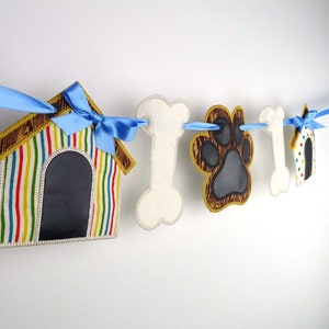 May include: A colourful dog-themed banner featuring a dog house, bone, paw print, and a second dog house. The banner is strung with blue ribbon.