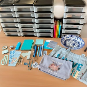 May include: A white ceramic mug with a black handle and the text "But First, Coffee" in a bold, black font. The mug is set against a blurred background, suggesting a cozy setting.