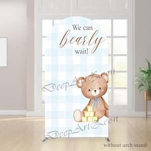 Op de afbeelding: Een baby shower boog achtergrond met een aquarel teddybeer met een blauwe strik, zittend naast houten blokken. De achtergrond heeft een blauw-wit ruitpatroon en de tekst "We can bearly wait!"