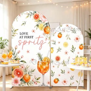May include: Two arched backdrop panels featuring a white background with watercolor illustrations of oranges, grapefruits, lemons, and pink flowers. The larger panel displays the black and pink text "LOVE AT FIRST spritz" and a large cocktail glass.